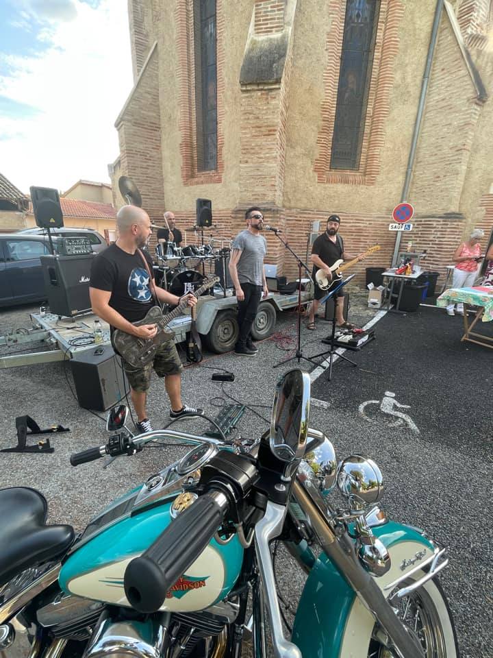 Concert en plein air sur la place du village, au pied de l’église, avec une moto garée au premier plan