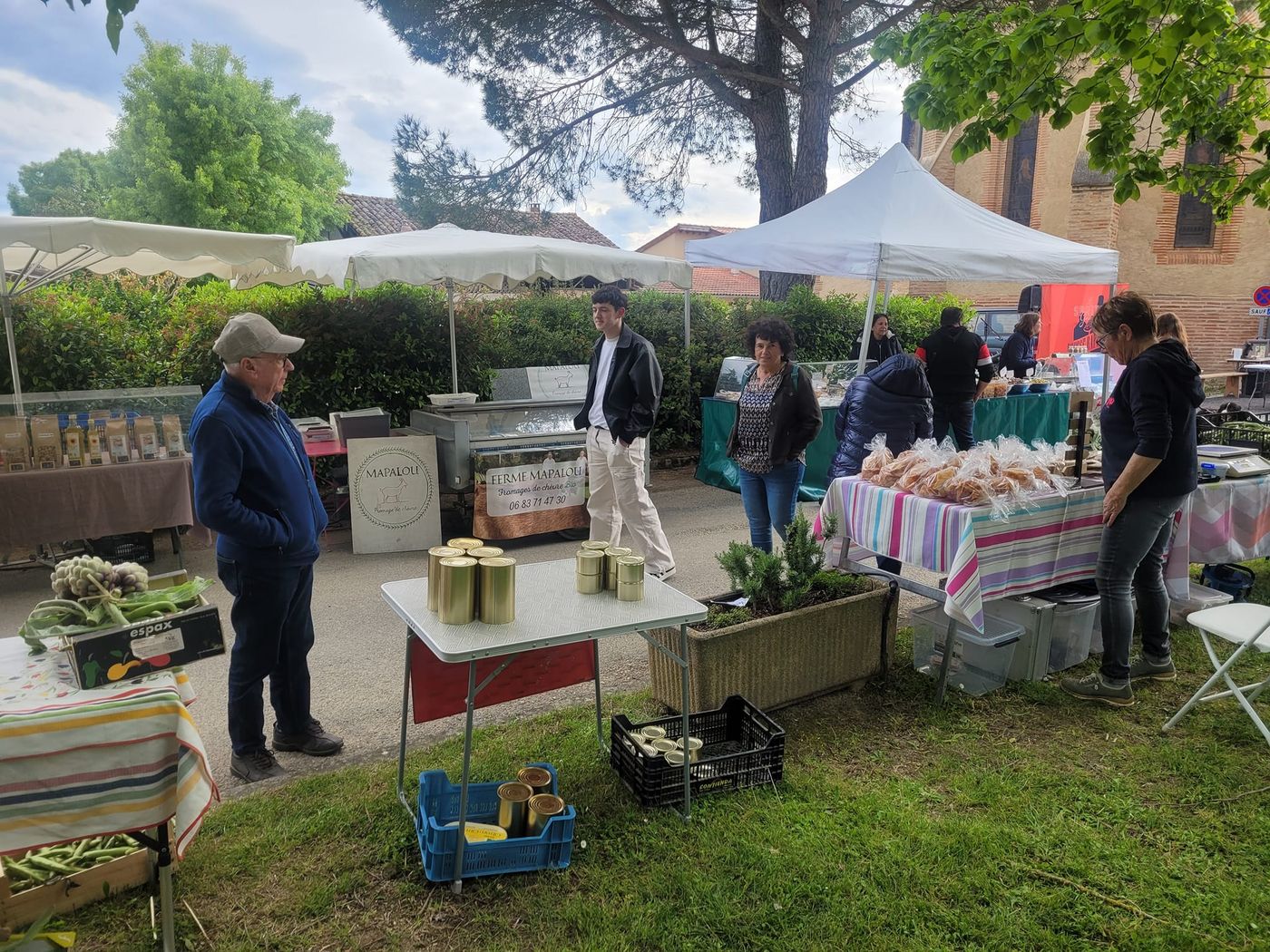 Étals de producteurs sous des barnums, sur l’herbe, avec bocaux et légumes en cagettes