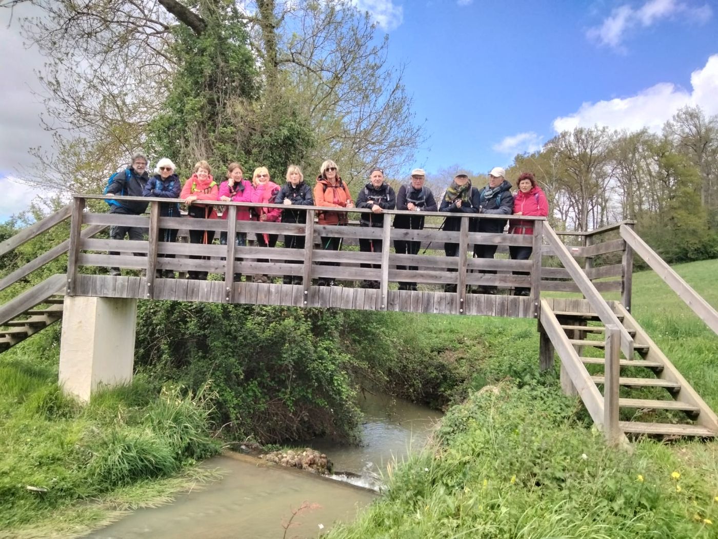 Groupe de marcheurs alignés sur une passerelle en bois au-dessus d’un ruisseau