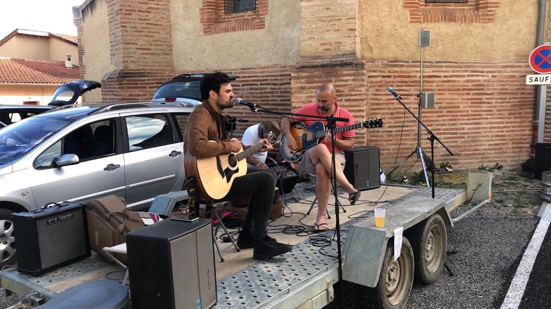 Deux guitaristes jouent sur une remorque faisant office de scène, devant un mur de brique